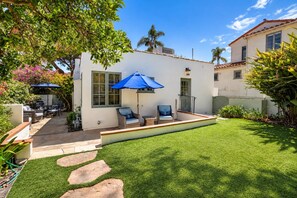 A patio with outdoor furniture and a blue umbrella, surrounded by a well-maintained lawn and stone steps. - New! Casa Capricho in West Beach with A/C, private yard, walk to beach (Santa Barbara)