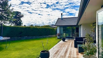 Ein modernes Haus mit Holzterrasse, kleinem Garten und blauem Himmel.
