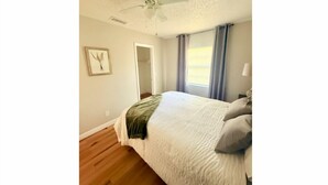 Ein Schlafzimmer mit Bett, Deckenventilator, Tür und Fenster mit Vorhängen.