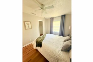 A bedroom with a bed, a ceiling fan, a door, and a window with curtains. - Cozy 3BR Retreat • Seminole Heights Gem (Tampa)