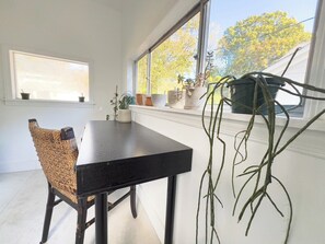 Ein Essbereich mit Tisch und Stühlen, Blumentöpfen und einem Fenster mit Blick auf Bäume.