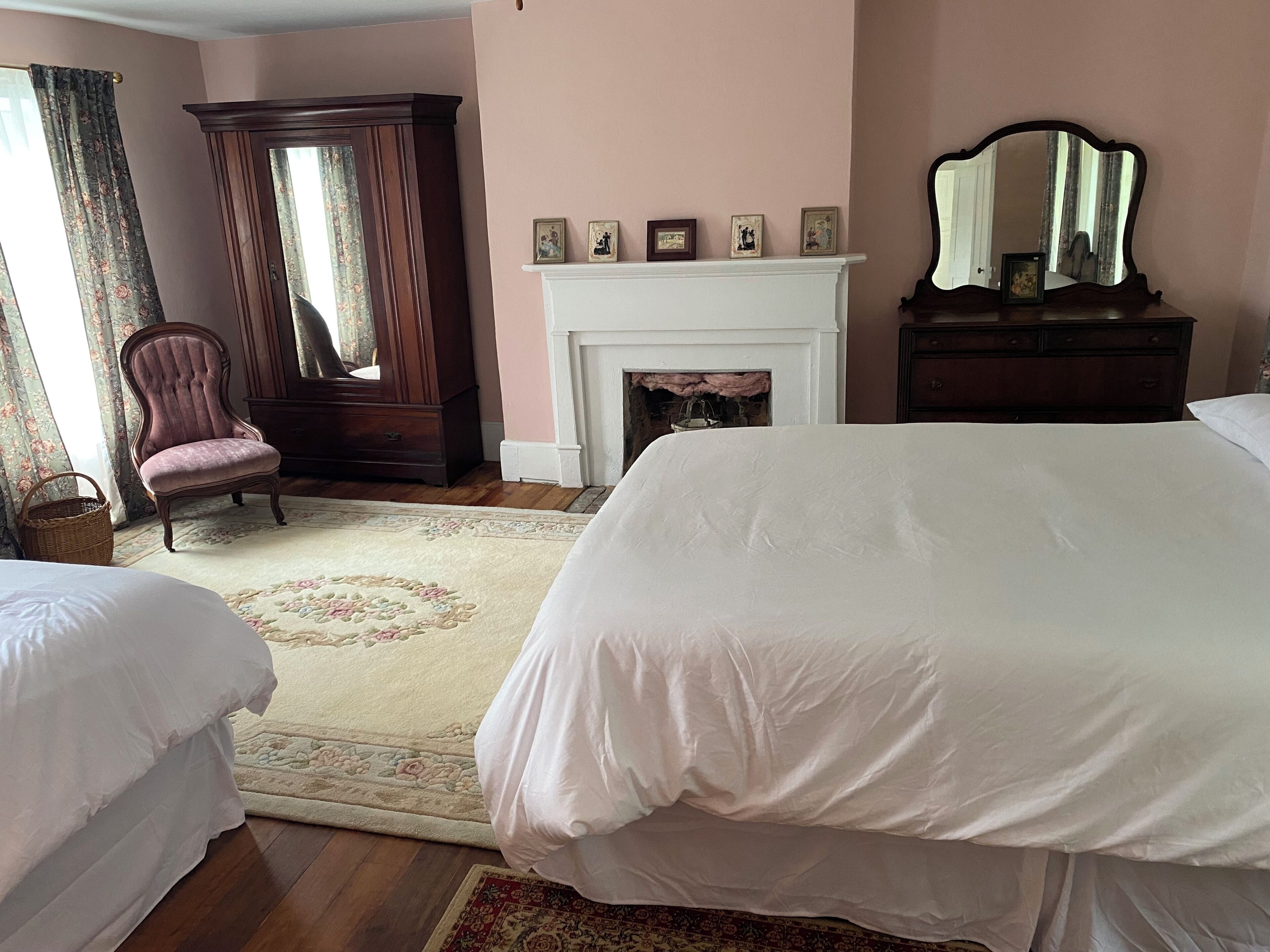 A bedroom with two beds, a fireplace, a mirror, and a chair.