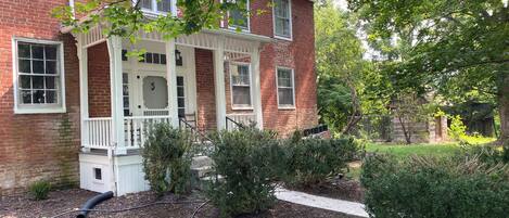 A brick house with a porch, a small garden, and a pathway.