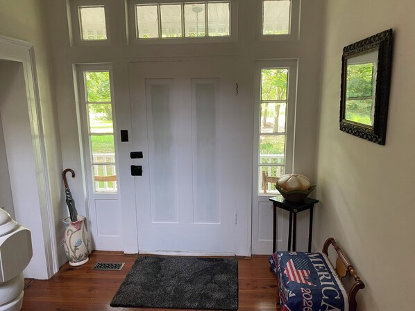 Una habitación con una puerta blanca, una pequeña mesa con un globo terráqueo, un banco con diseño de bandera estadounidense y una ventana con vistas a zonas verdes.
