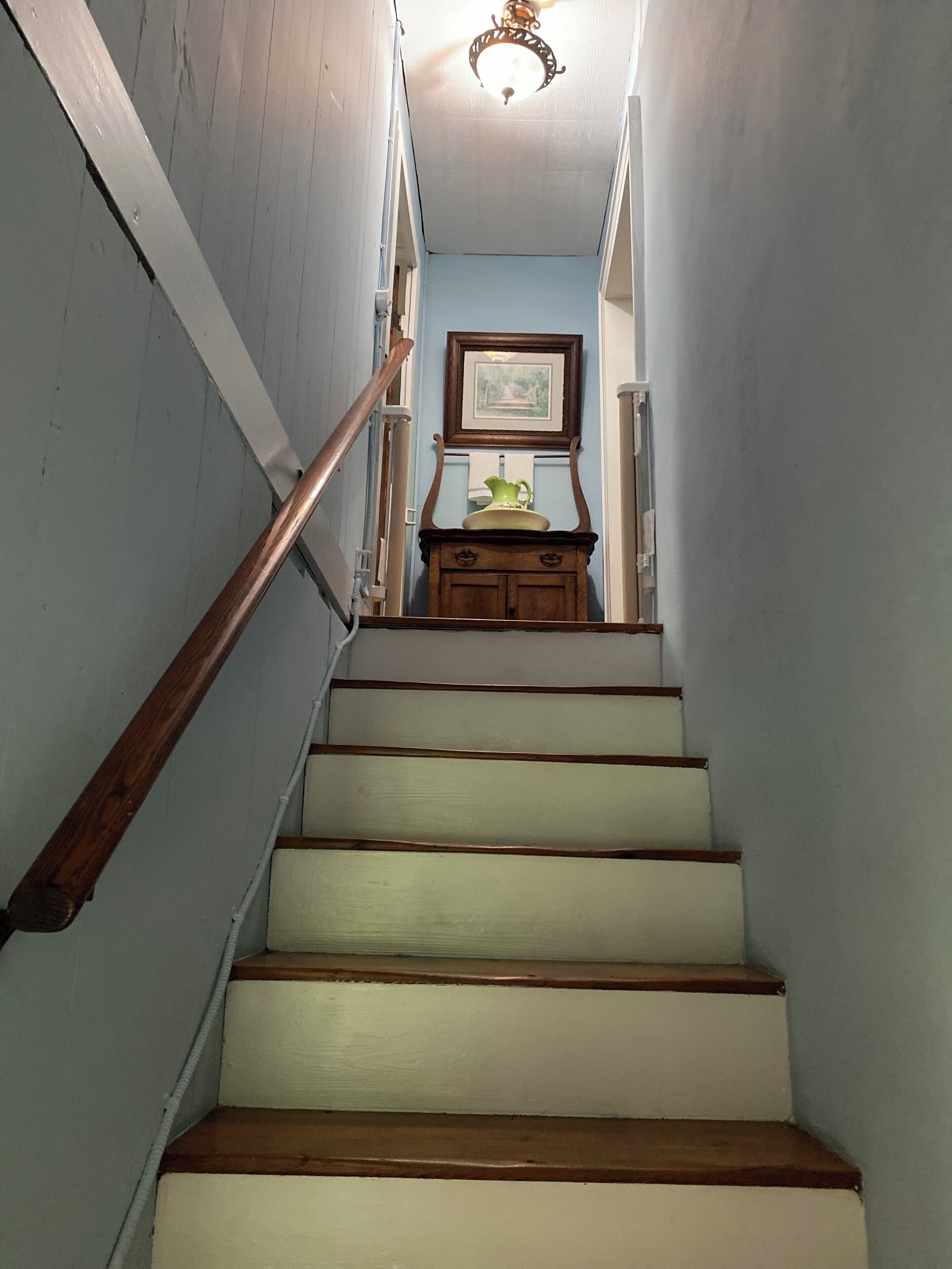 A staircase with wooden handrails, a light fixture, and a framed picture on the wall.