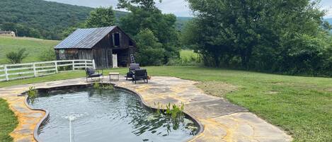 A rustic outdoor setting with a stone patio, a small pond, and a wooden barn.