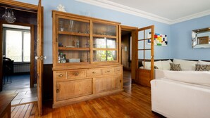 Een kamer met houten vloer, een witte bank, een houten kast met glazen deuren en een spiegel aan de muur.