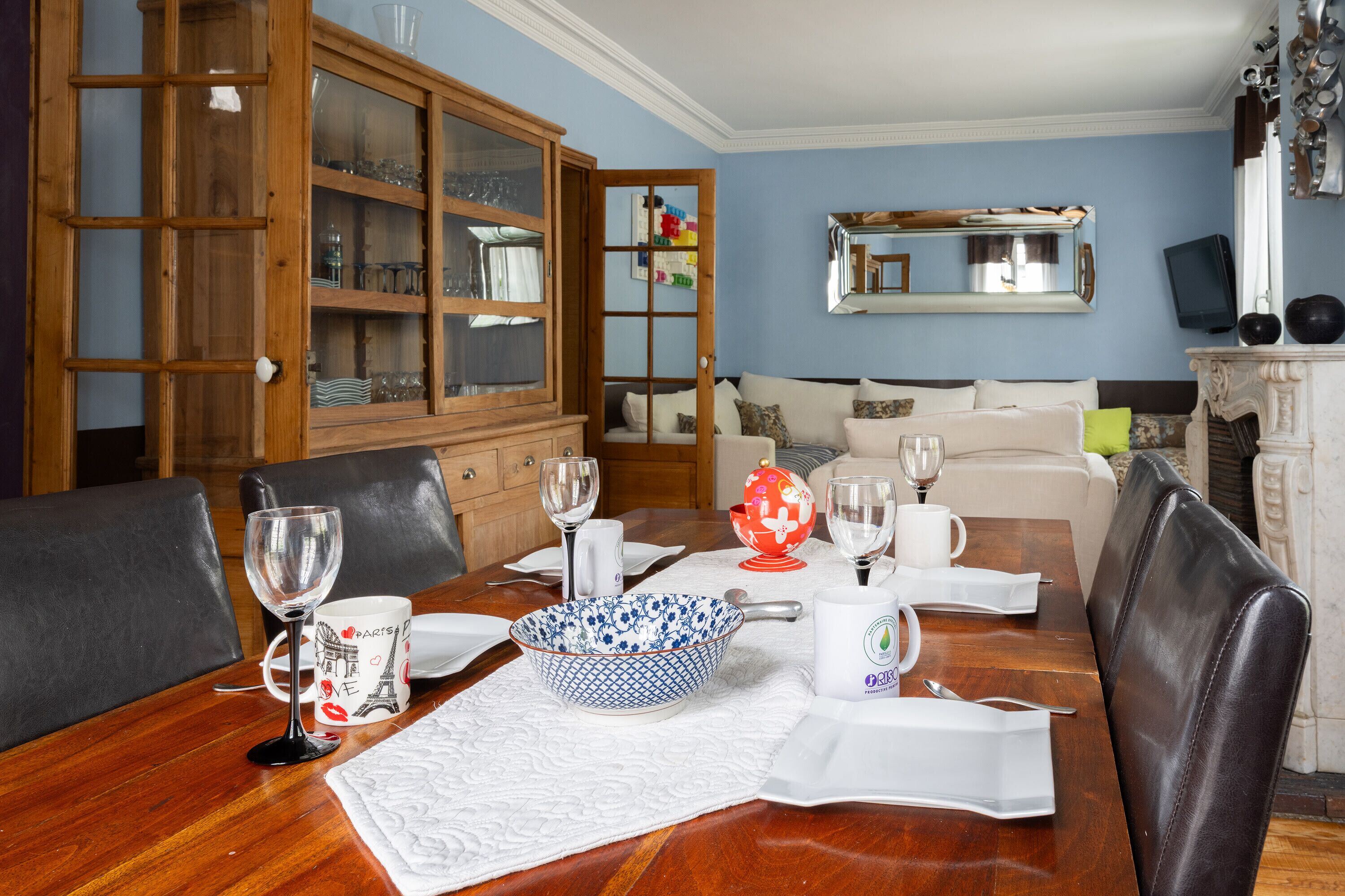 A dining area with a wooden table, chairs, a cabinet with glass doors, a sofa, and a fireplace.