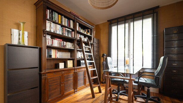 Een kamer met een houten bureau, een boekenkast, een ladder en een stoel.