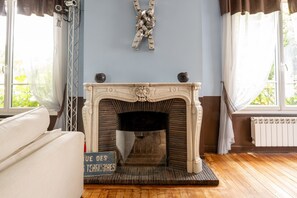 A room with a fireplace, a sofa, and a window with curtains. - L'Oasis Familiale Arborée - Welkeys (Vincennes)