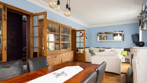 Een eetgedeelte met een houten tafel, stoelen, een kast met glazen deuren, een witte bank en een spiegel aan de muur.