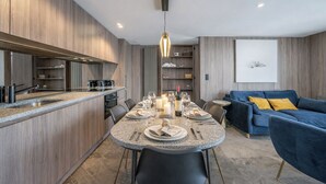 A modern kitchen with a dining area, a blue sofa, and a mounted artwork on the wall. - L'Écrin des Cristaux avec balcon - Welkeys (Megève)