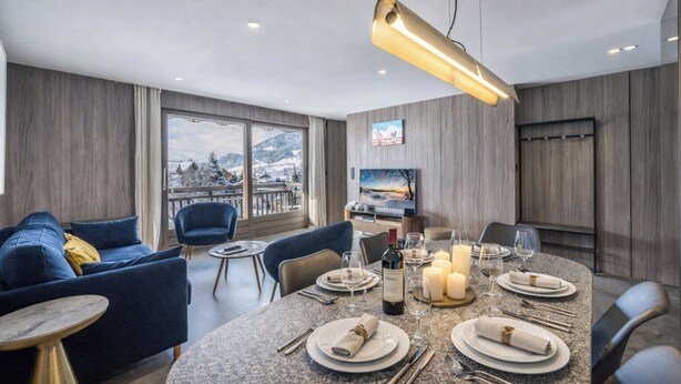 A modern dining area with a table set for four, a sofa, and a TV in the background. - L'Écrin des Cristaux avec balcon - Welkeys (Megève)