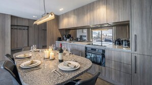 A modern kitchen with granite countertops, a dining area with a round table set for four, and a view of the outdoors through a large window. - L'Écrin des Cristaux avec balcon - Welkeys (Megève)