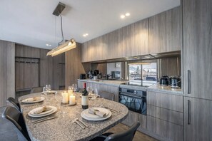 Eine moderne Küche mit Granit-Arbeitsplatten, ein Essbereich mit rundem Tisch für vier Personen und ein Blick ins Freie durch ein großes Fenster.