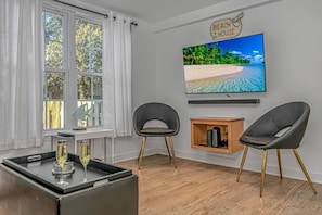 A living room with a TV, two chairs, a small wooden cabinet, and a window with curtains. - 7BR Family Oasis | Heated Pool + Walk to Beach (North Myrtle Beach)