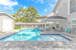 A backyard with a rectangular swimming pool, a covered patio area, and a fenced yard. - 7BR Family Oasis | Heated Pool + Walk to Beach (North Myrtle Beach)
