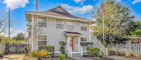 A two-story house with a front porch, a flagpole, and a picket fence.