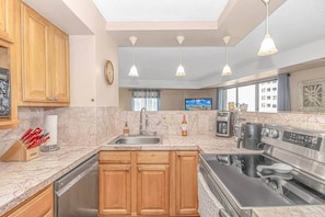 A modern kitchen with wooden cabinets, a stainless steel stove, a coffee maker, and a TV in the background. - Updated 3BR w/ Oceanviews on MB Boardwalk! (Myrtle Beach)