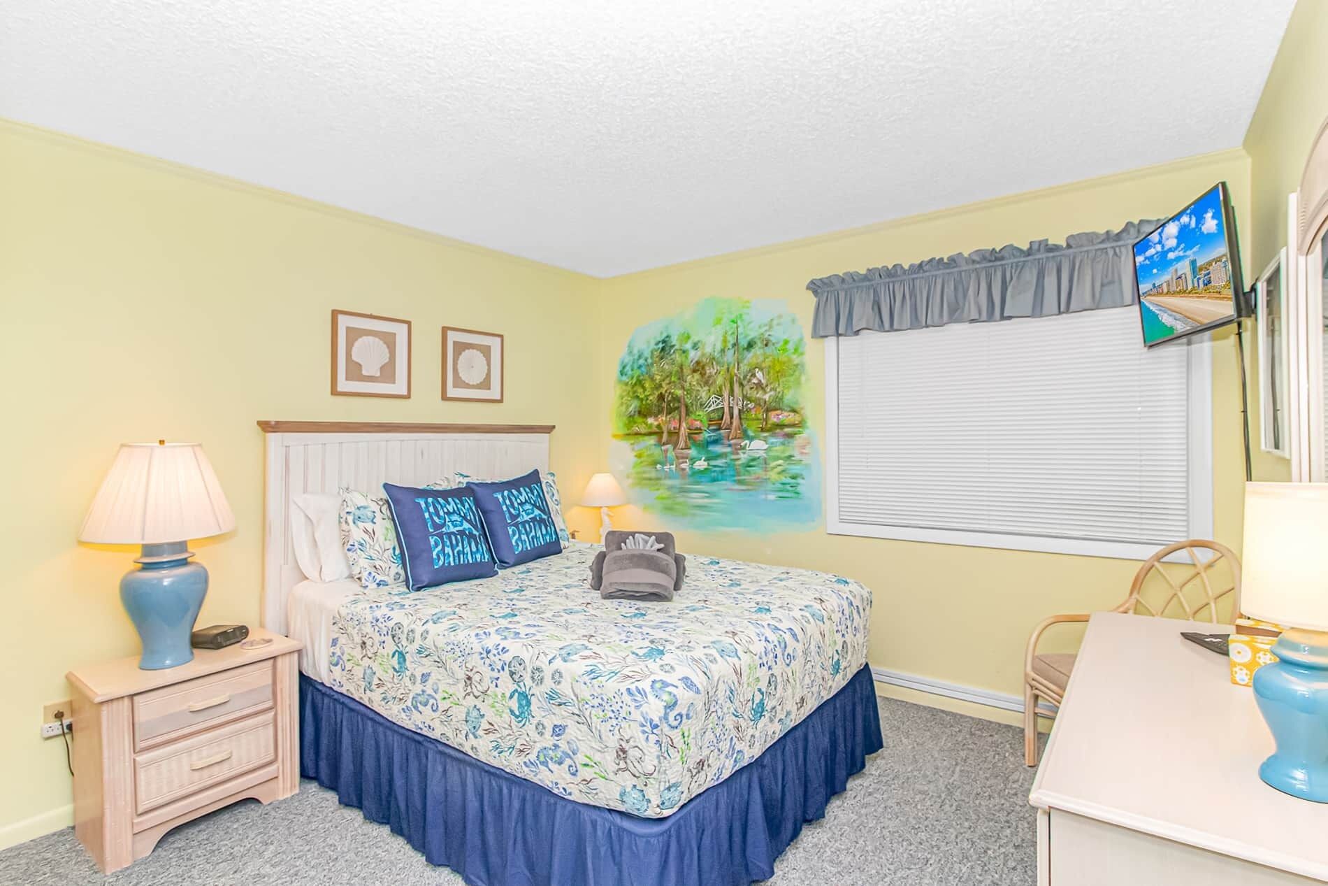 A bedroom with a bed, bedside tables, a desk, a chair, and a window with blinds.