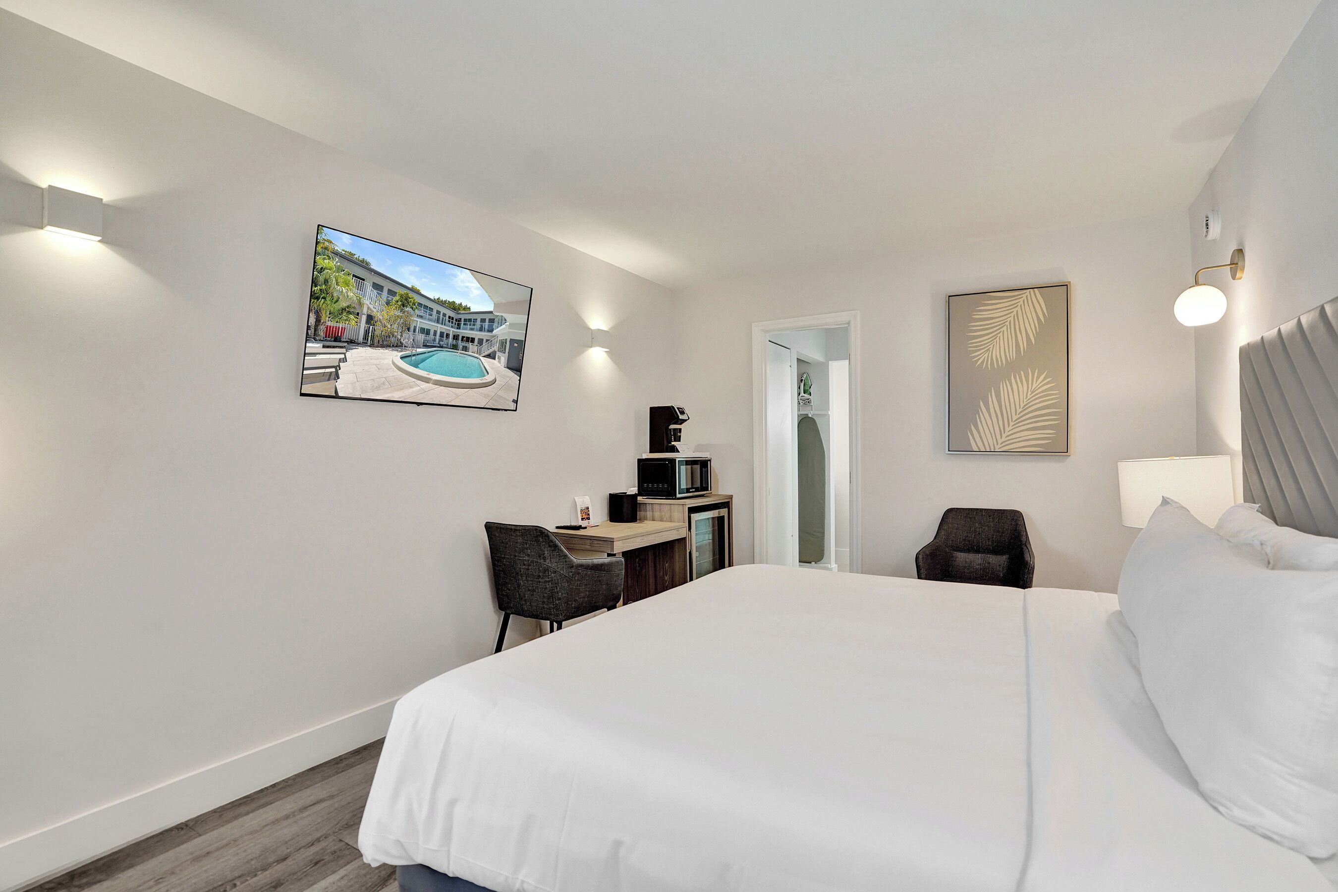 Una habitación de hotel con cama, escritorio, silla y un cuadro de una piscina en la pared.