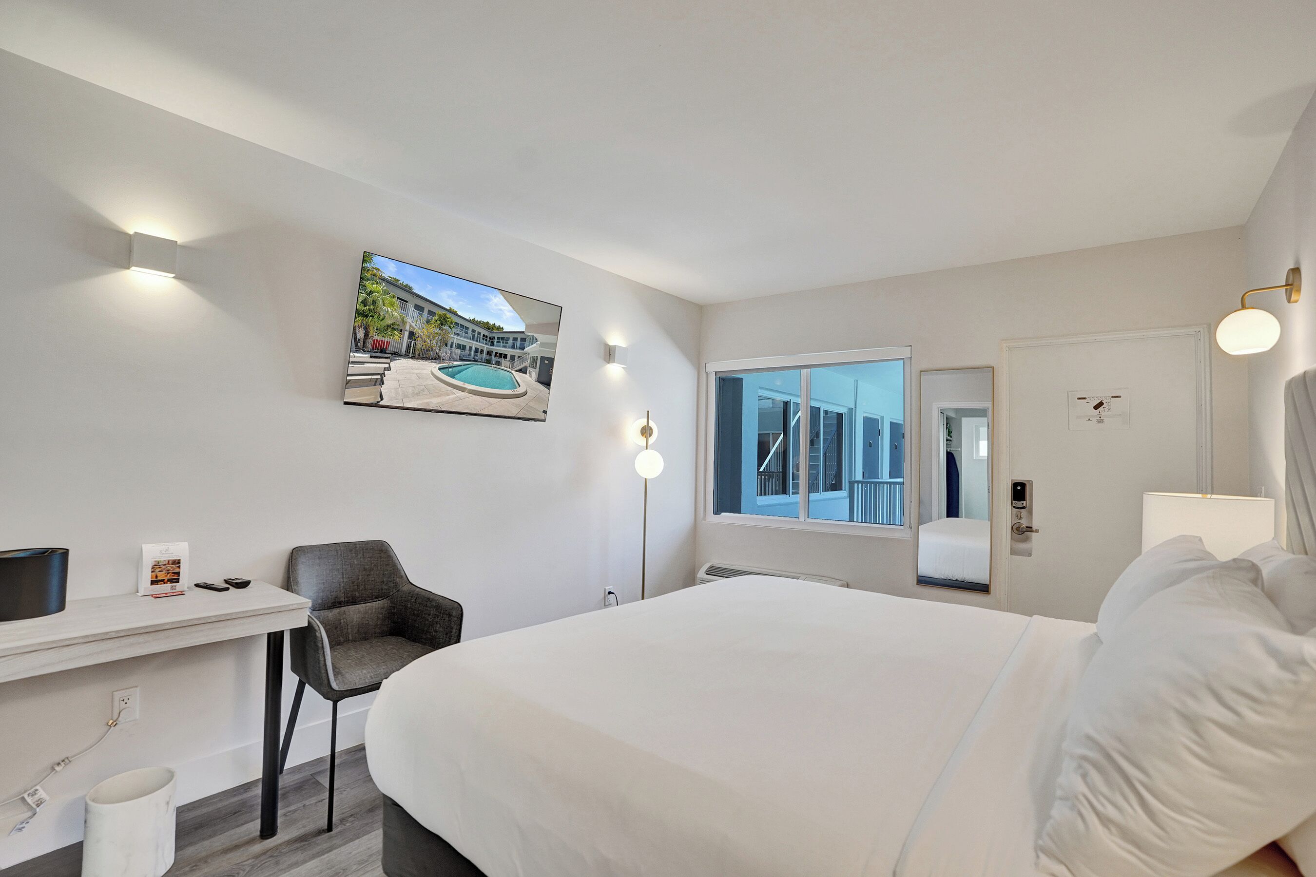 Habitación de hotel con cama, escritorio, silla y un ventanal con vista a un edificio.