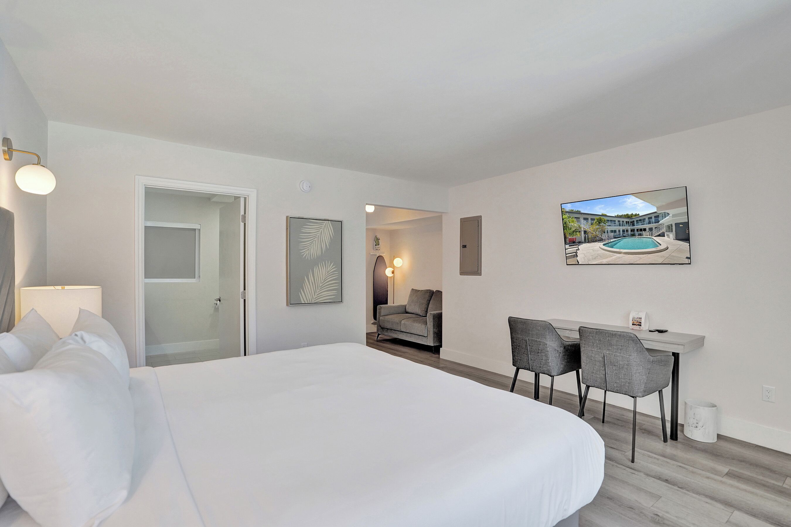 A hotel room with a bed, a desk, two chairs, a framed picture, and a door leading to a bathroom.
