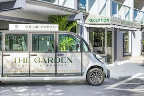 Uma van branca com a marca 'The Garden Hotel & Resort', estacionada em frente a um edifício com a placa 'Reception'.