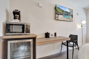 Habitació d'hotel amb petita cuina, televisió penjada a la paret, llit i escriptori amb cadira.