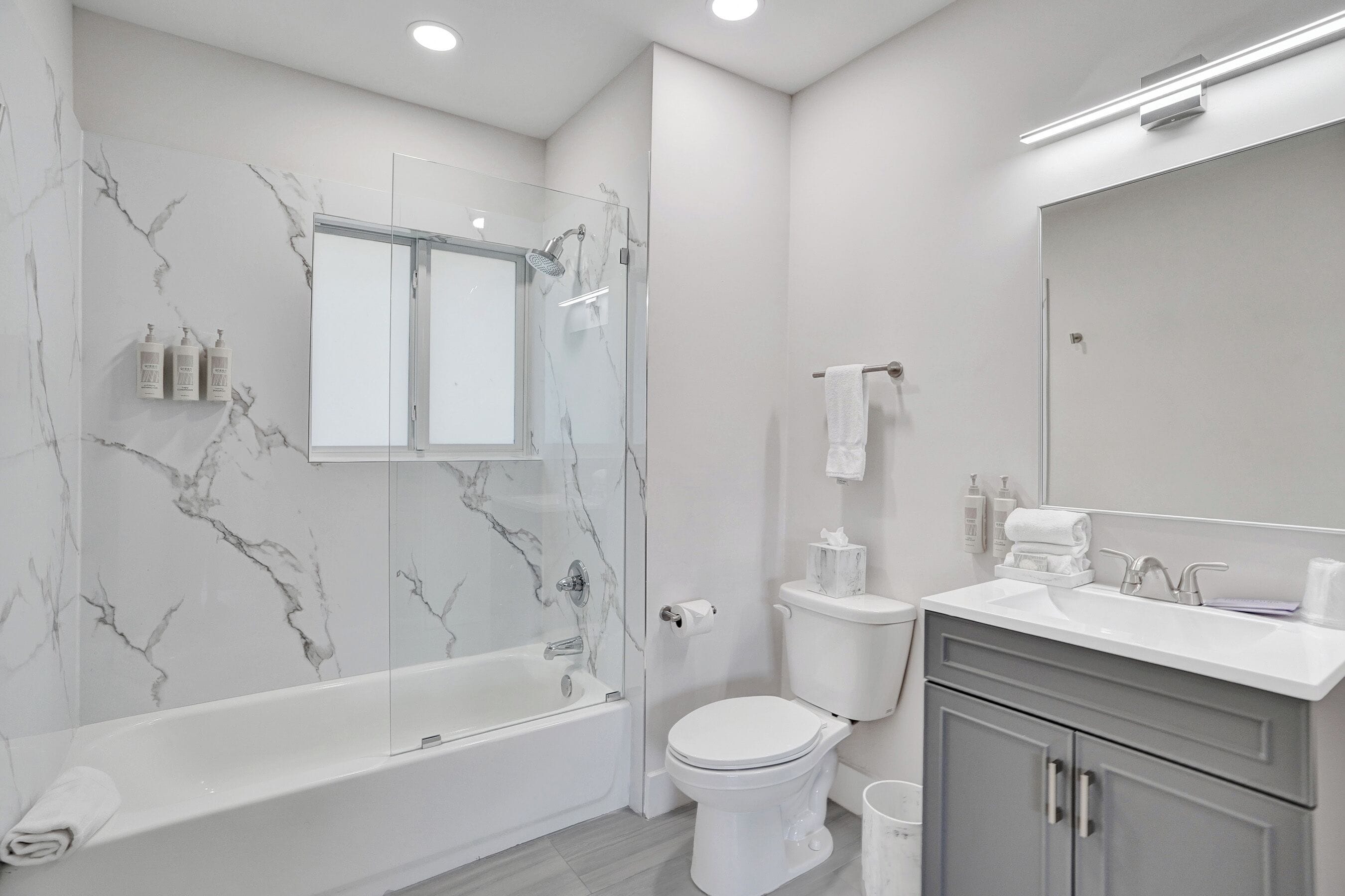 A modern bathroom with a marble wall, a glass shower enclosure, a white toilet, and a vanity with a mirror.