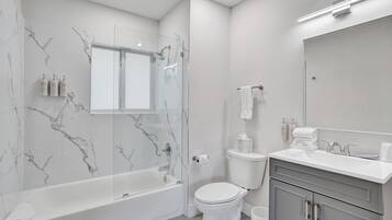 A modern bathroom with a marble wall, a glass shower enclosure, a white toilet, and a vanity with a mirror.