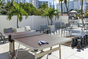 Uma mesa de pingue-pongue com rede, cercada por assentos externos e peças de xadrez.