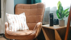 Una silla de cuero marrón con un cojín estampado, un vaso negro y una planta en maceta sobre una mesa de madera.