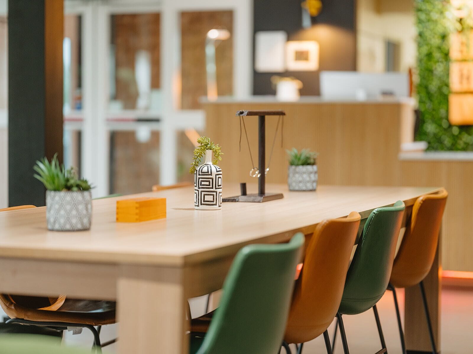 Un comedor moderno con una mesa de madera, sillas verdes y marrones, y plantas decorativas.