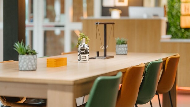 Un comedor moderno con una mesa de madera, sillas verdes y marrones, y plantas decorativas.