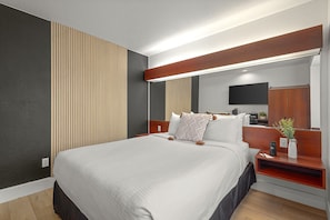Een moderne hotelkamer met een groot bed, een houten hoofdbord, een nachtkastje met een lamp, een spiegel en een televisie.
