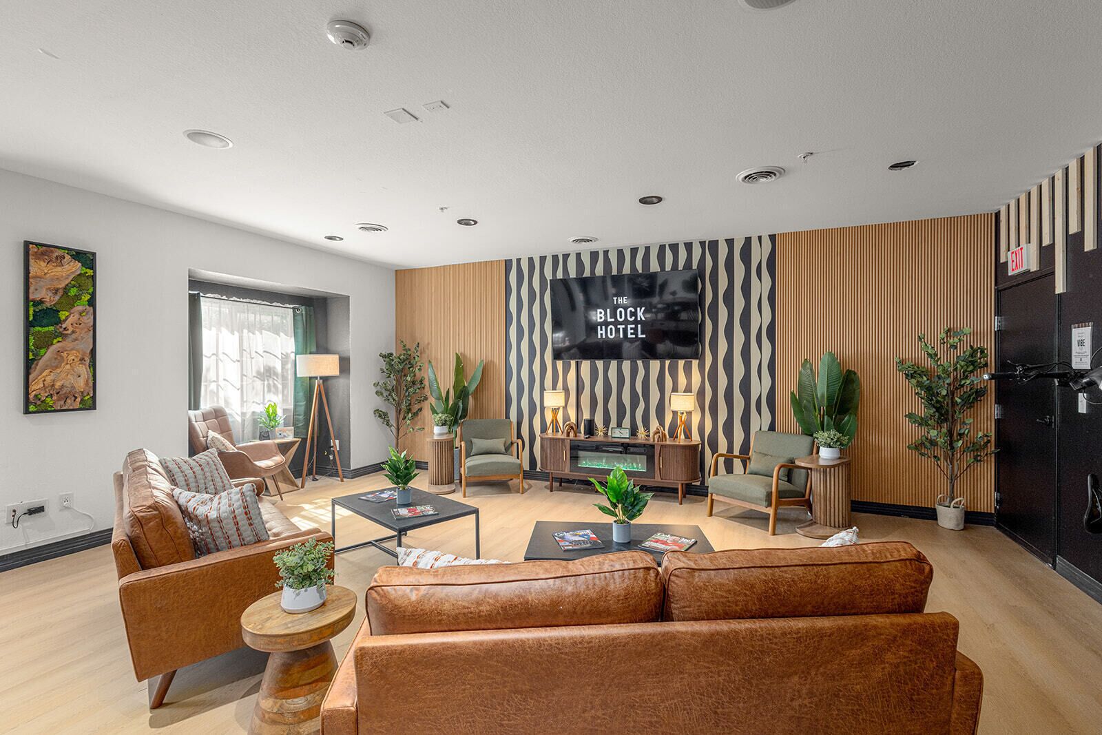 A modern hotel living room with leather sofas, a flat-screen TV, and a variety of plants.