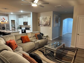 A living room with a sofa, coffee table, and a kitchen in the background. - Spacious 4BR Family Retreat Near Whitewater & Airport, pets allow (Charlotte)