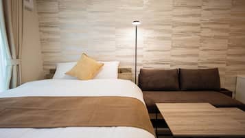 A hotel room with a bed, a sofa, a bedside table, and a floor lamp.
