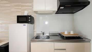 A compact kitchen with a microwave, refrigerator, sink, and a small countertop with a tray holding two cups.
