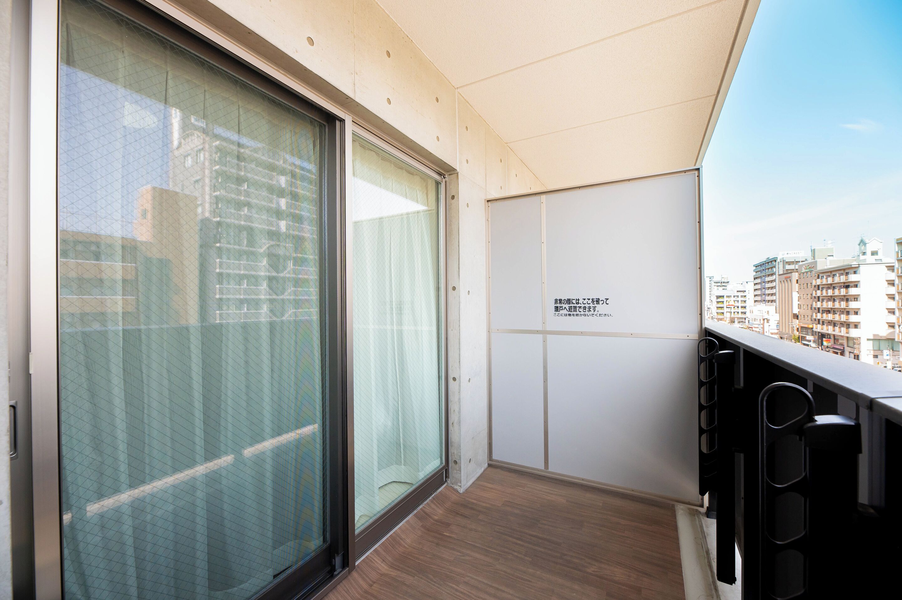Un balcon avec vue sur la ville, une porte-fenêtre coulissante et un mur blanc orné d’une enseigne.