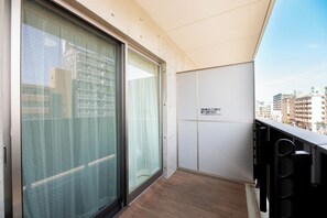 A balcony with a view of the city, a sliding glass door, and a white wall with a sign.