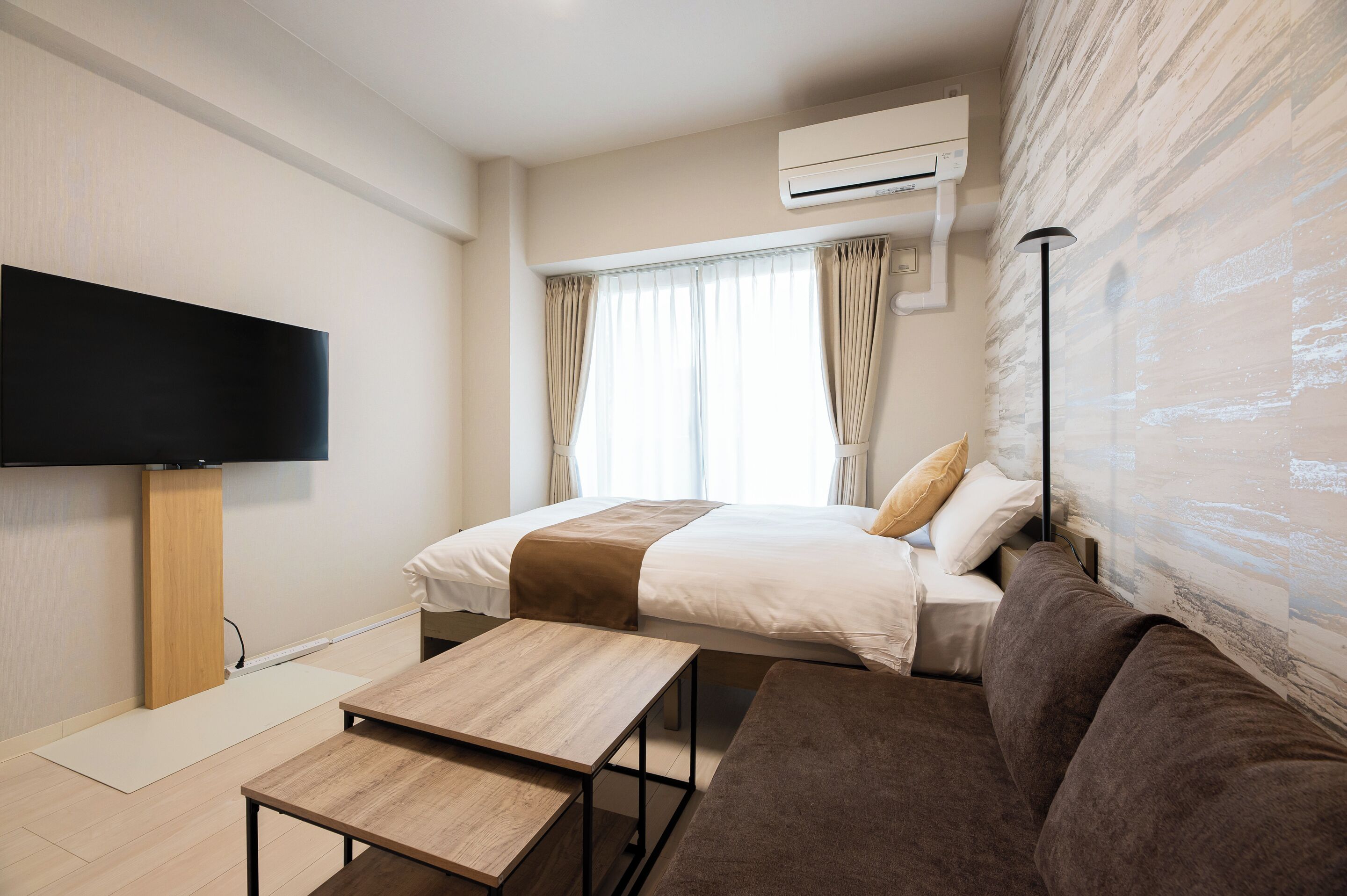 Ein Hotelzimmer mit Bett, einer Sitzecke, einem Fernseher, einer Klimaanlage und einem fenster mit Vorhängen.