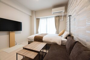 A hotel room with a bed, a sofa, a TV, an air conditioner, and a window with curtains. - ESTRELA Ogusu (Fukuoka City Minami ku)