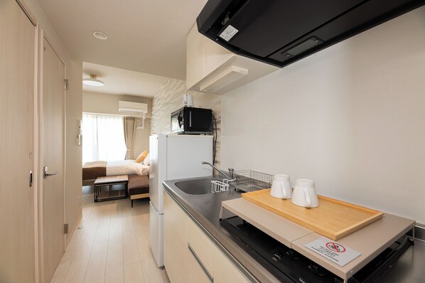 A compact kitchen with a microwave, sink, and a small dining area with a cutting board and cups.