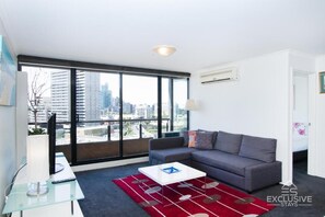 Uma sala de estar moderna com um sofá cinzento, uma mesa de centro branca e um tapete vermelho.