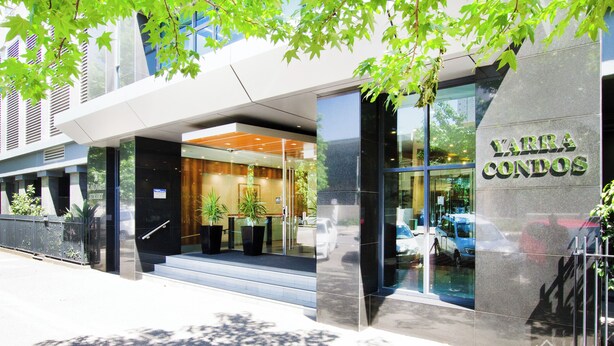 A modern building with a glass entrance, a sign reading "YARRA CONDOS," and a staircase leading to the entrance. - Exclusive Stays - Yarra Condos (Southbank)