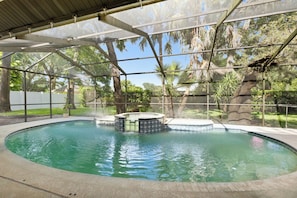 Ein überdachter Pool mit Whirlpool, umgeben von Bäumen und einem weißen Zaun.