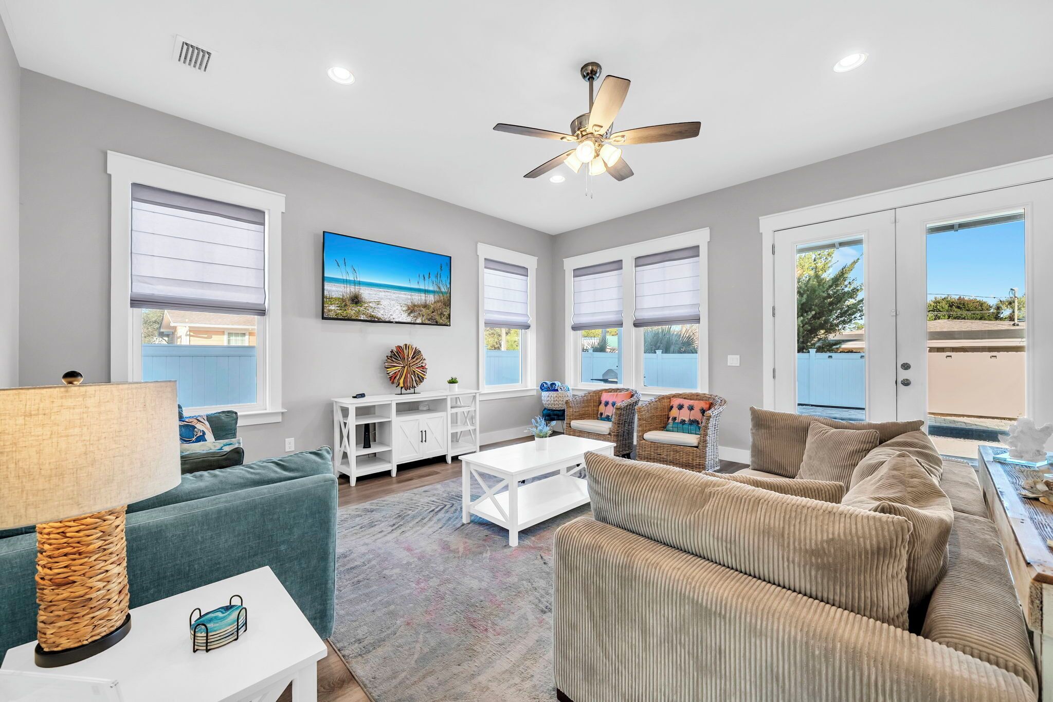 A spacious living room with a ceiling fan, large windows, a sofa, a coffee table, and a TV.