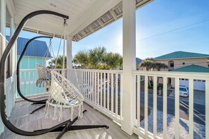 A porch with a hammock chair, a white railing, and a view of a street with a car and buildings. - Panama City Beach, FL | 6BR | 4.5BA | Sleeps 18 | Private Pool | Dog-Friendly (Panama City Beach)